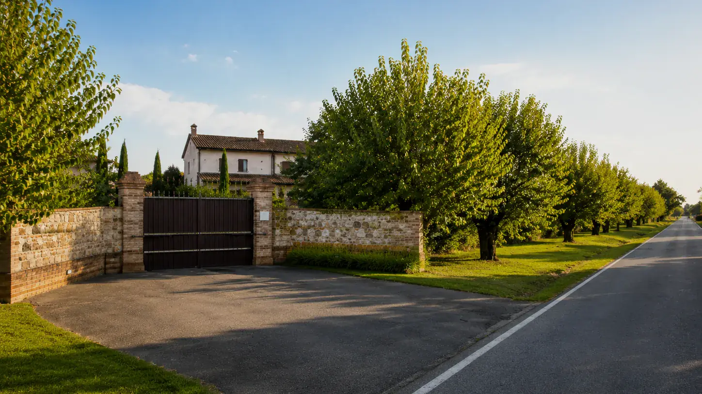 Cancello d'ingresso della tenuta, muro in pietra e mattone sulla strada alberata